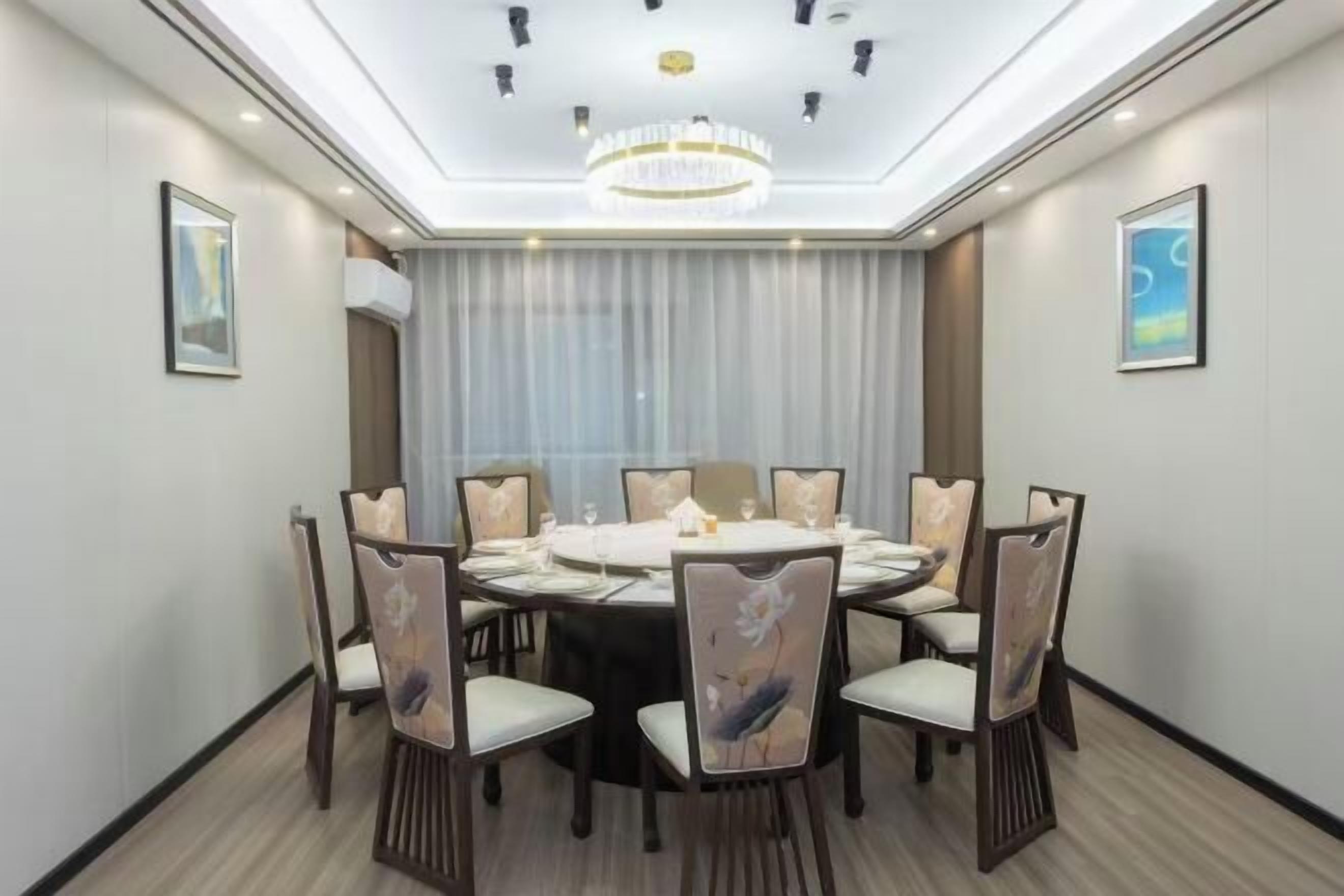 A dining area with a round table, eight chairs, and a chandelier.