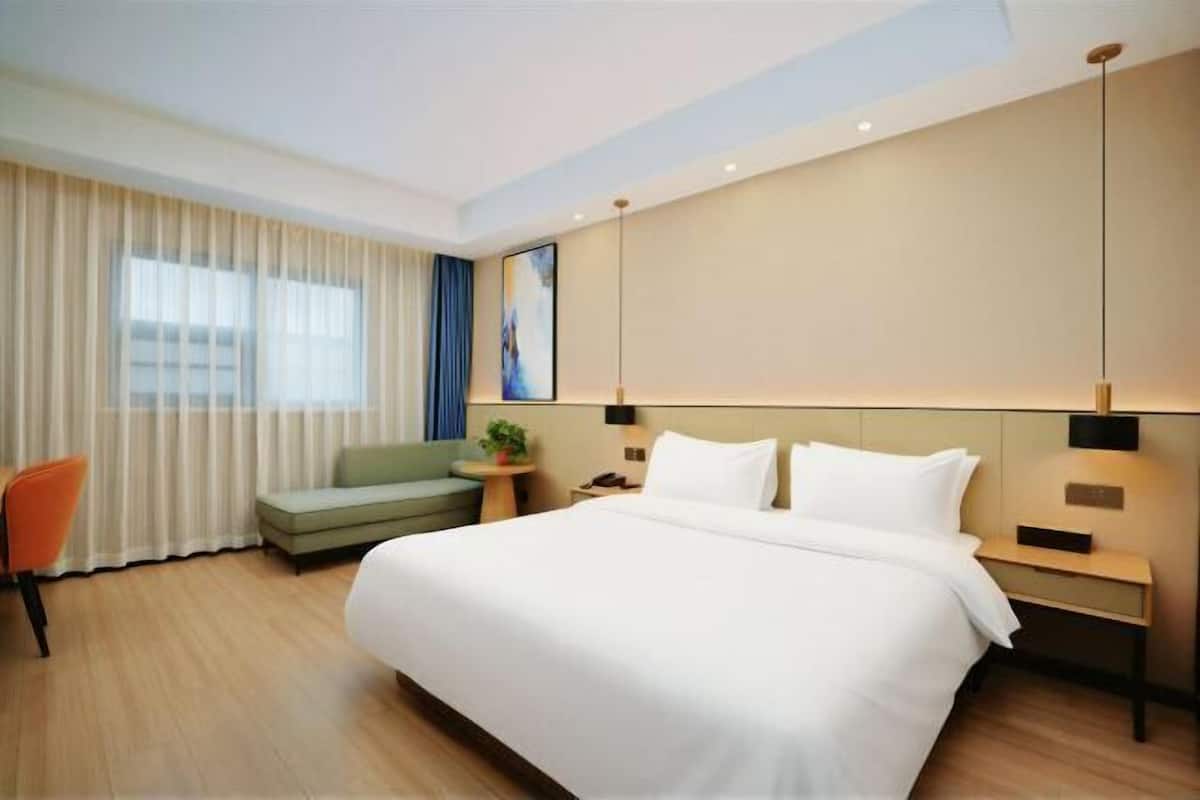 Habitación de hotel con una cama grande, un sofá, una silla, una mesita de noche y una mesilla.