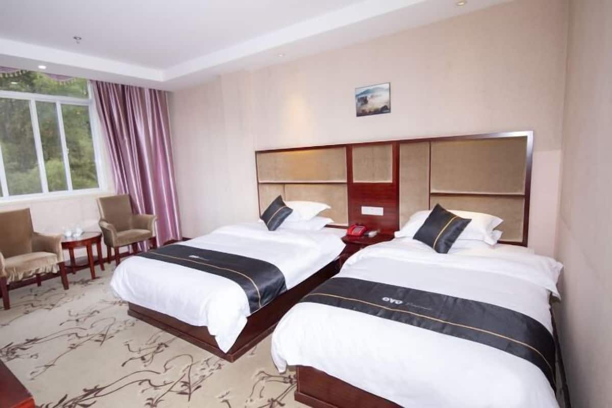 Habitación de hotel con dos camas, un escritorio, una silla y una ventana con cortinas.