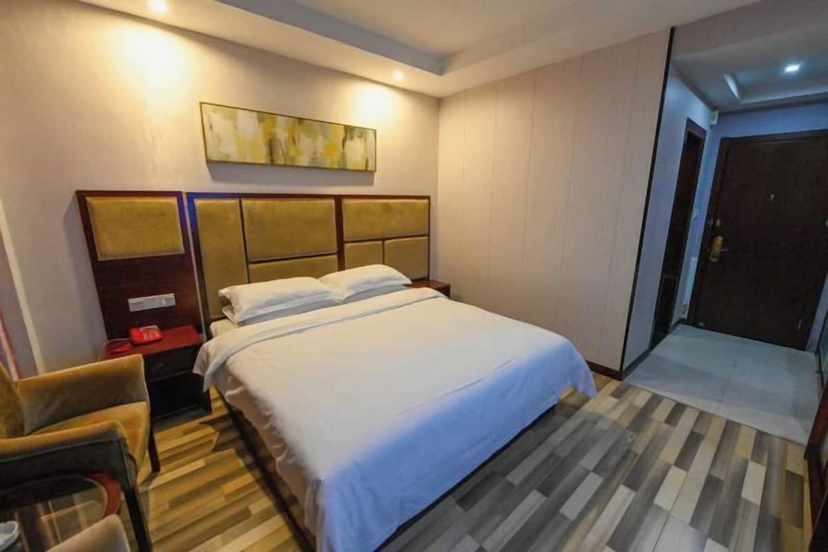 Habitación de hotel con cama, mesita de noche, silla, un cuadro en la pared y una puerta.