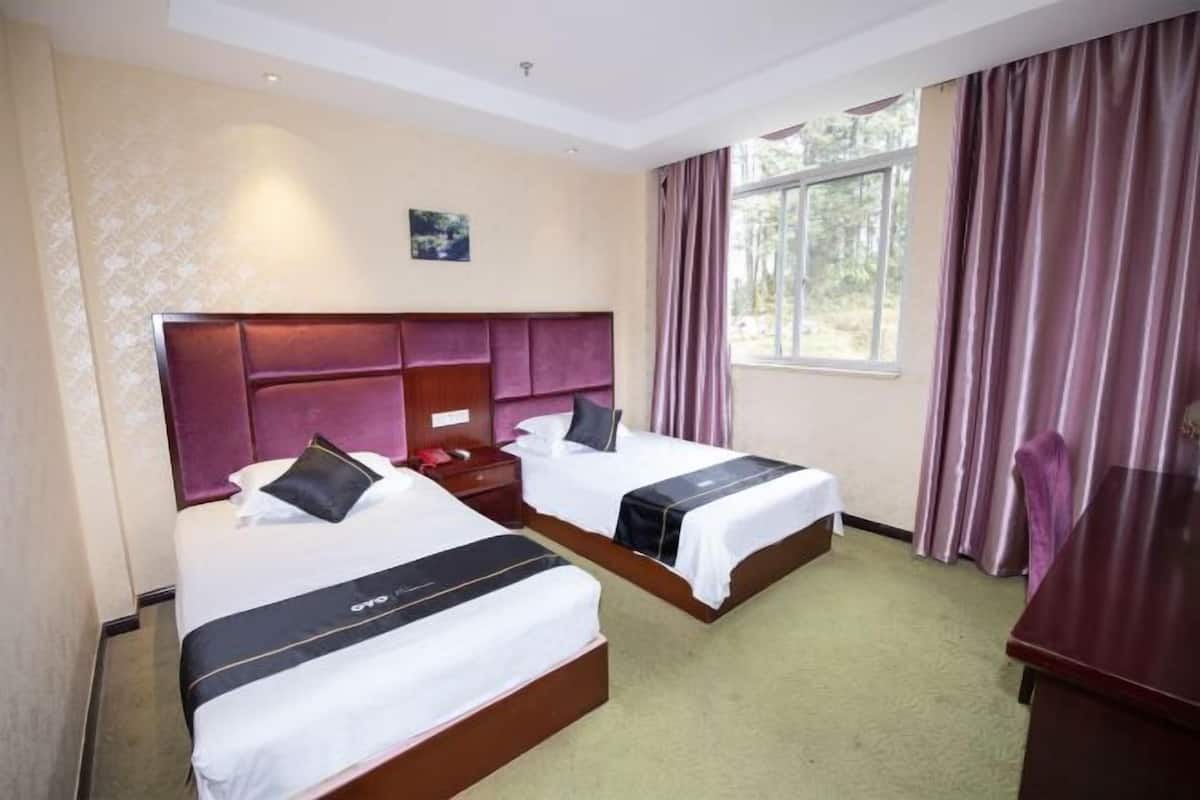 Habitación de hotel con dos camas, cabecero de madera, escritorio y ventana con cortinas.