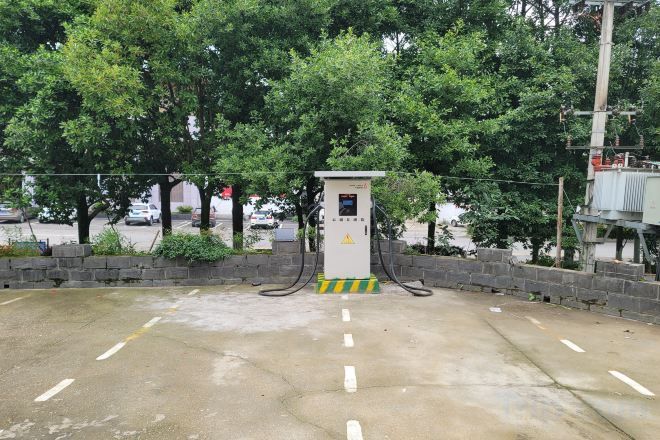 Una stazione di servizio con un piccolo chiosco, immersa nel verde e circondata da un'area pavimentata con linee bianche.