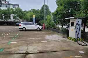 Un estacionamiento con un coche blanco y una estación de carga para vehículos eléctricos.