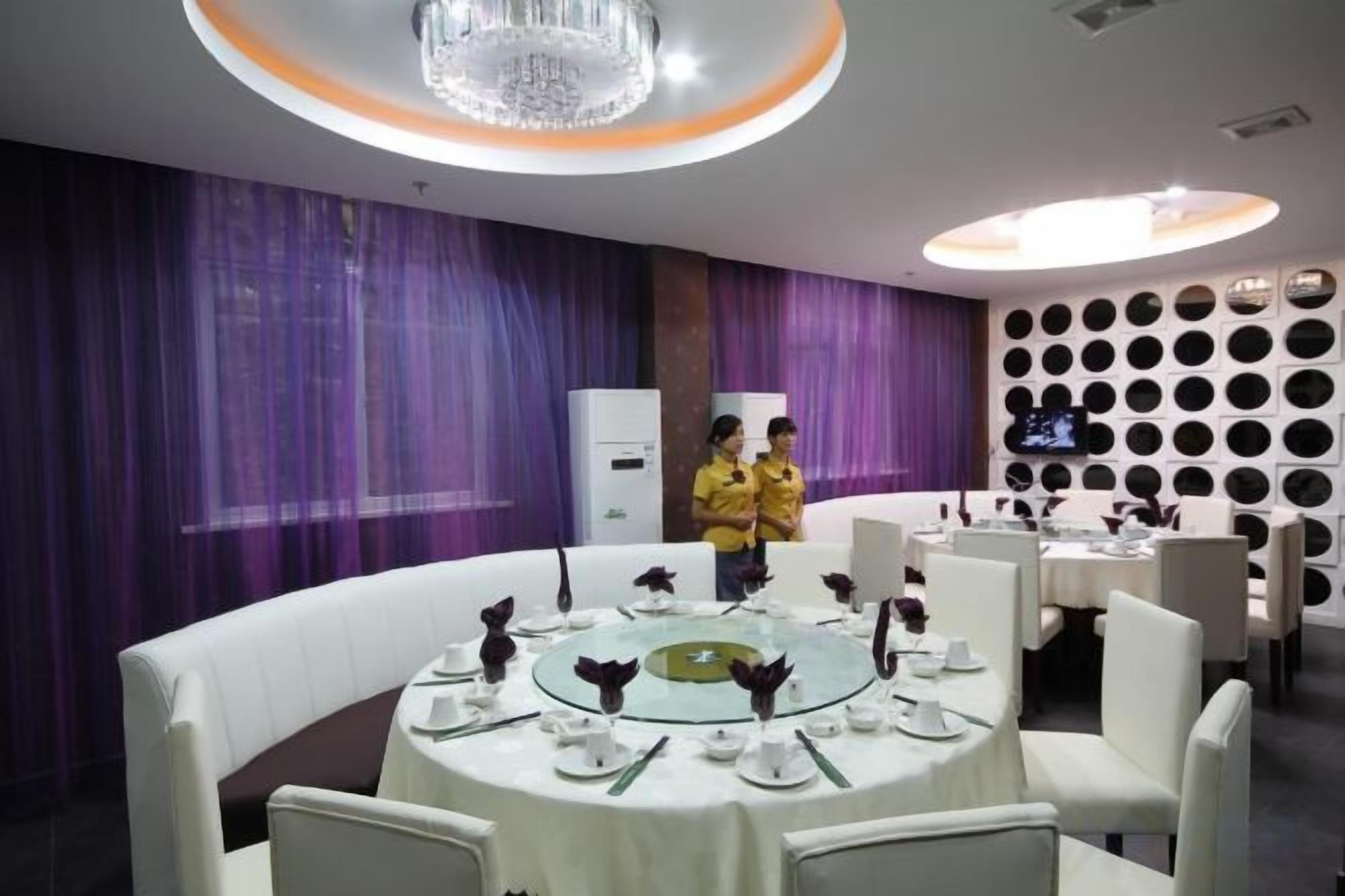A dining area with round tables, white chairs, and purple curtains.