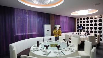 A dining area with round tables, white chairs, and purple curtains.