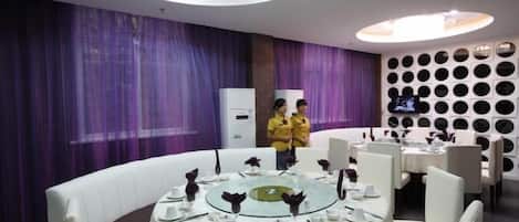 Un comedor con mesas redondas, sillas blancas y cortinas moradas.