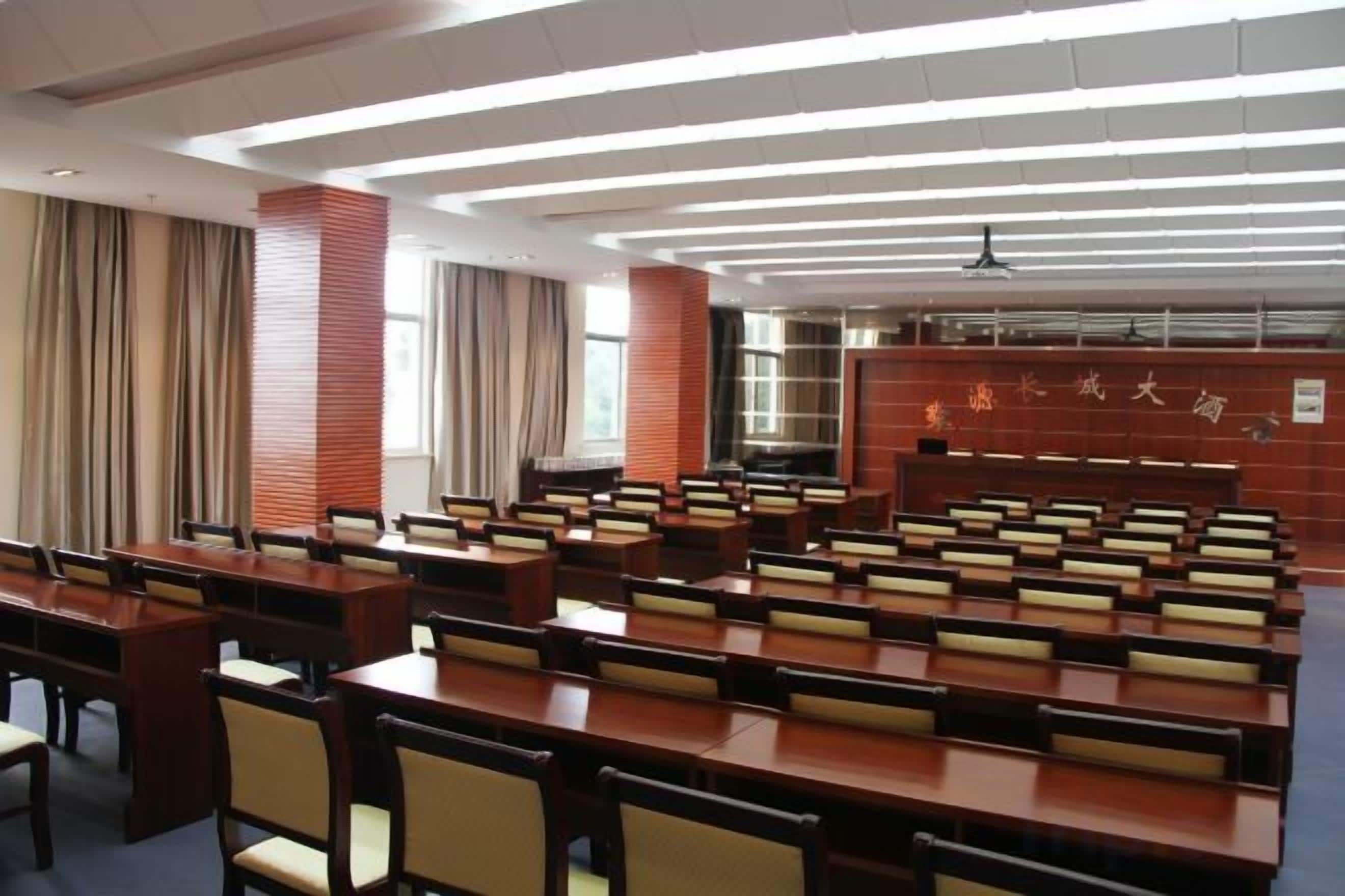 A conference room with multiple tables and chairs, a high ceiling with linear lighting, and a brick wall with Chinese characters.