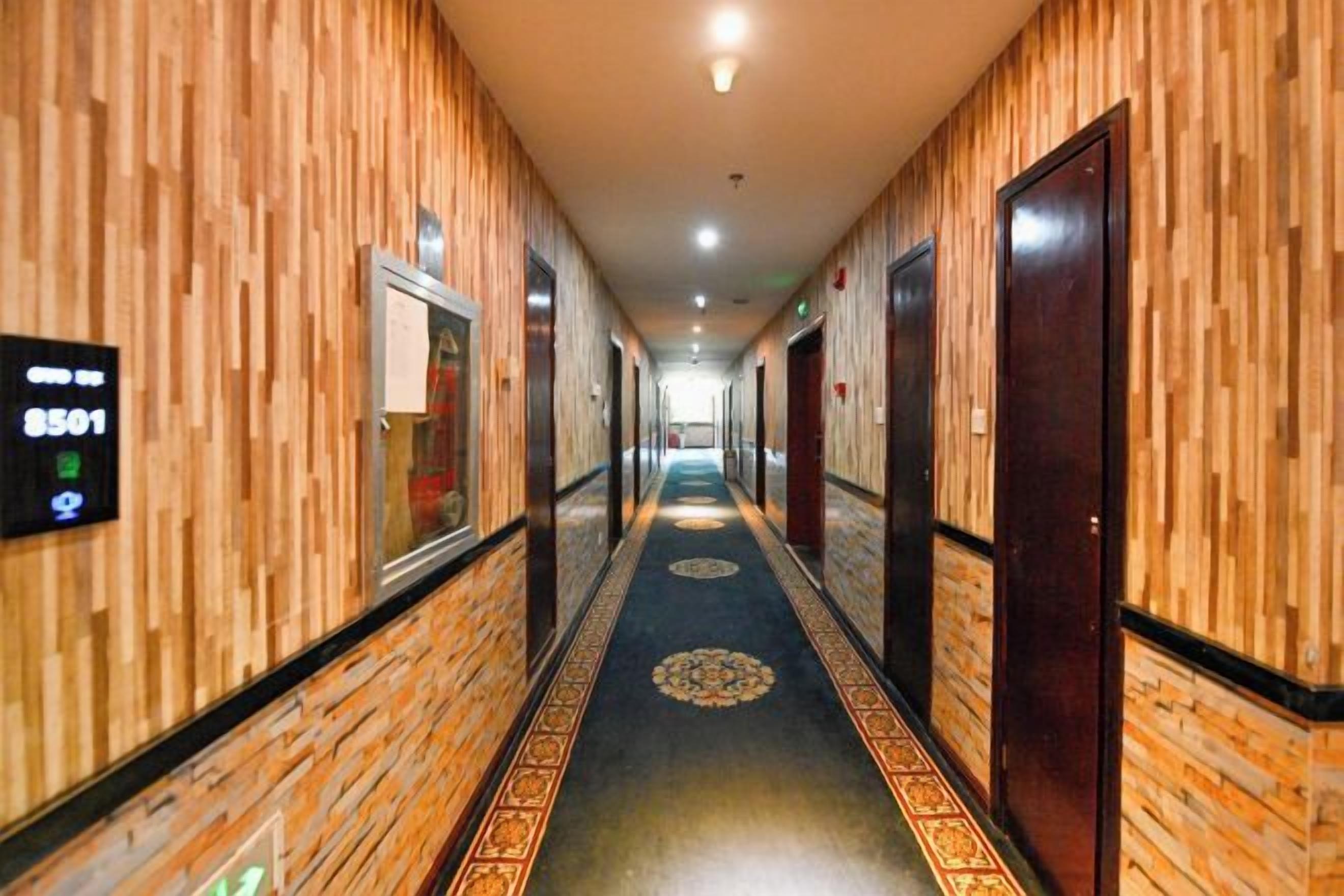 Un corridoio d'albergo con rivestimenti in legno, tappeto decorato e porte su entrambi i lati.