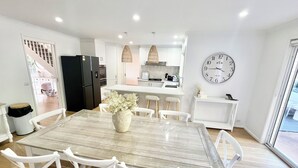 A modern kitchen with white cabinets, a black refrigerator, and a dining area with a marble table and white chairs. - SERENITY STAYS: Best price for value - 5 min from beach, cafes and racecourse (Mount Martha)