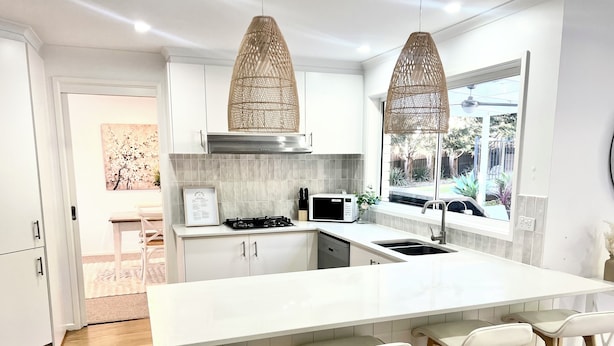 A modern kitchen with white cabinetry, a large island with bar stools, a gas stove, and a microwave. - SERENITY STAYS: Best price for value - 5 min from beach, cafes and racecourse (Mount Martha)