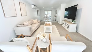 A modern living room with a sofa, coffee table, and TV. - SERENITY STAYS: Best price for value - 5 min from beach, cafes and racecourse (Mount Martha)