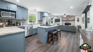 A modern kitchen with blue cabinets, a central island, and a dining area with a wooden table and bar stools. - Pet Friendly, Short walk to Lake Monroe (Nashville)