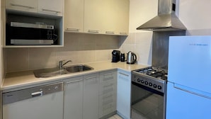 A modern kitchen with a dishwasher, stove, kettle, and a built-in oven.