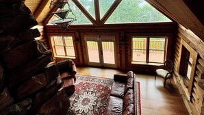 L’intérieur d’une cabane en rondins, avec un plafond en pente, une grande fenêtre, un canapé et un tapis à motifs.