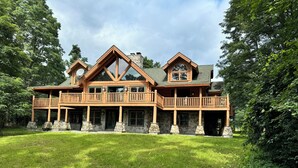 Une grande cabane en rondins à plusieurs étages, dotée de fondations en pierre, de nombreux balcons et d’une véranda qui fait le tour de la maison.