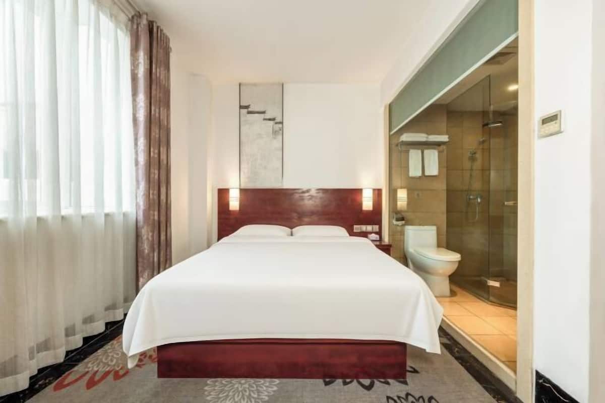 Una habitación de hotel con una cama, ducha y una puerta de vidrio que da al baño.