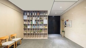 Un espace d’accueil avec une bibliothèque, deux chaises en bois et une porte sombre.