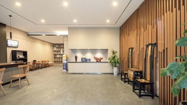 Un espace d’accueil moderne avec un comptoir de réception en bois, un coin salon et un grand miroir.