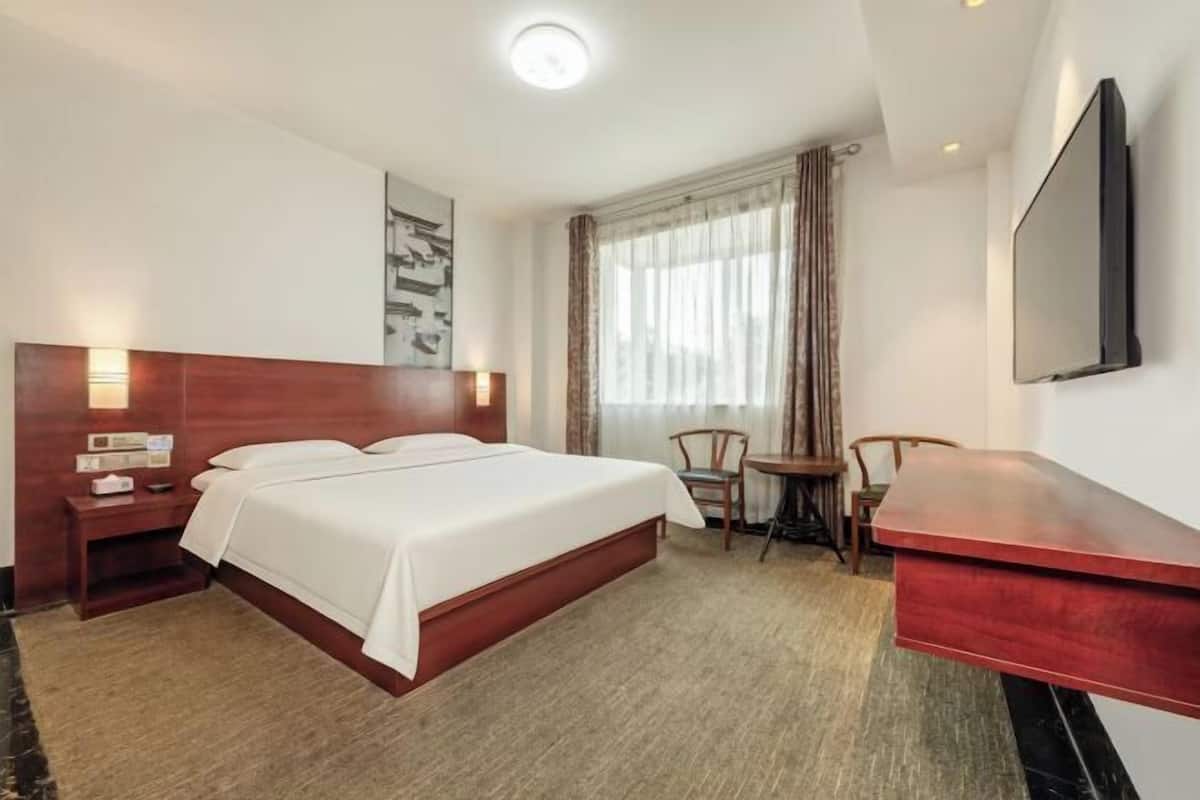 Habitación de hotel con cama, mesita de noche, escritorio, silla y televisor montado en la pared.