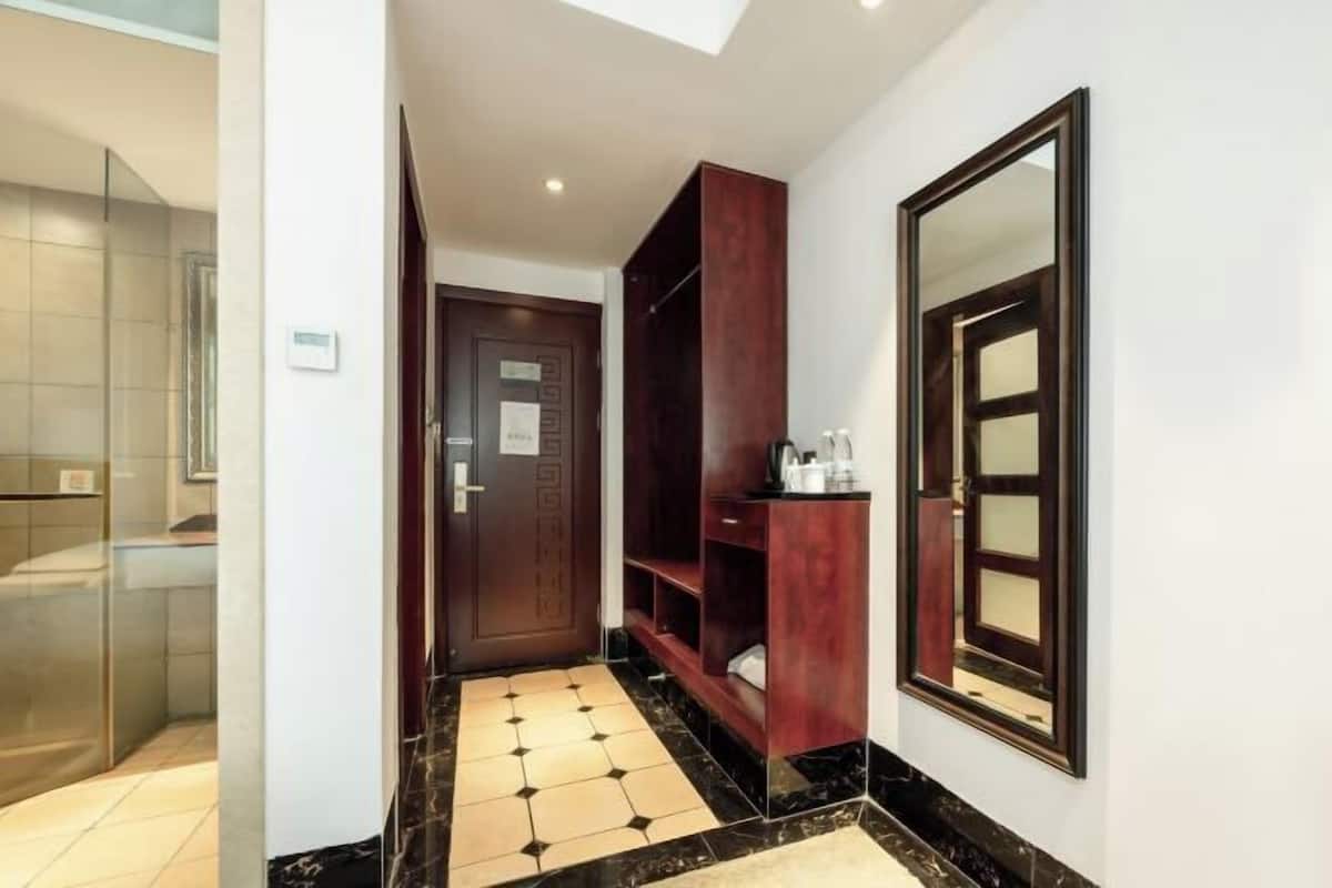 Un pasillo de hotel con una puerta, un armario de madera, un espejo y suelo de baldosas.