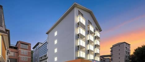 Un hotel de varios pisos con techo plano, varios balcones y entrada a nivel de calle.