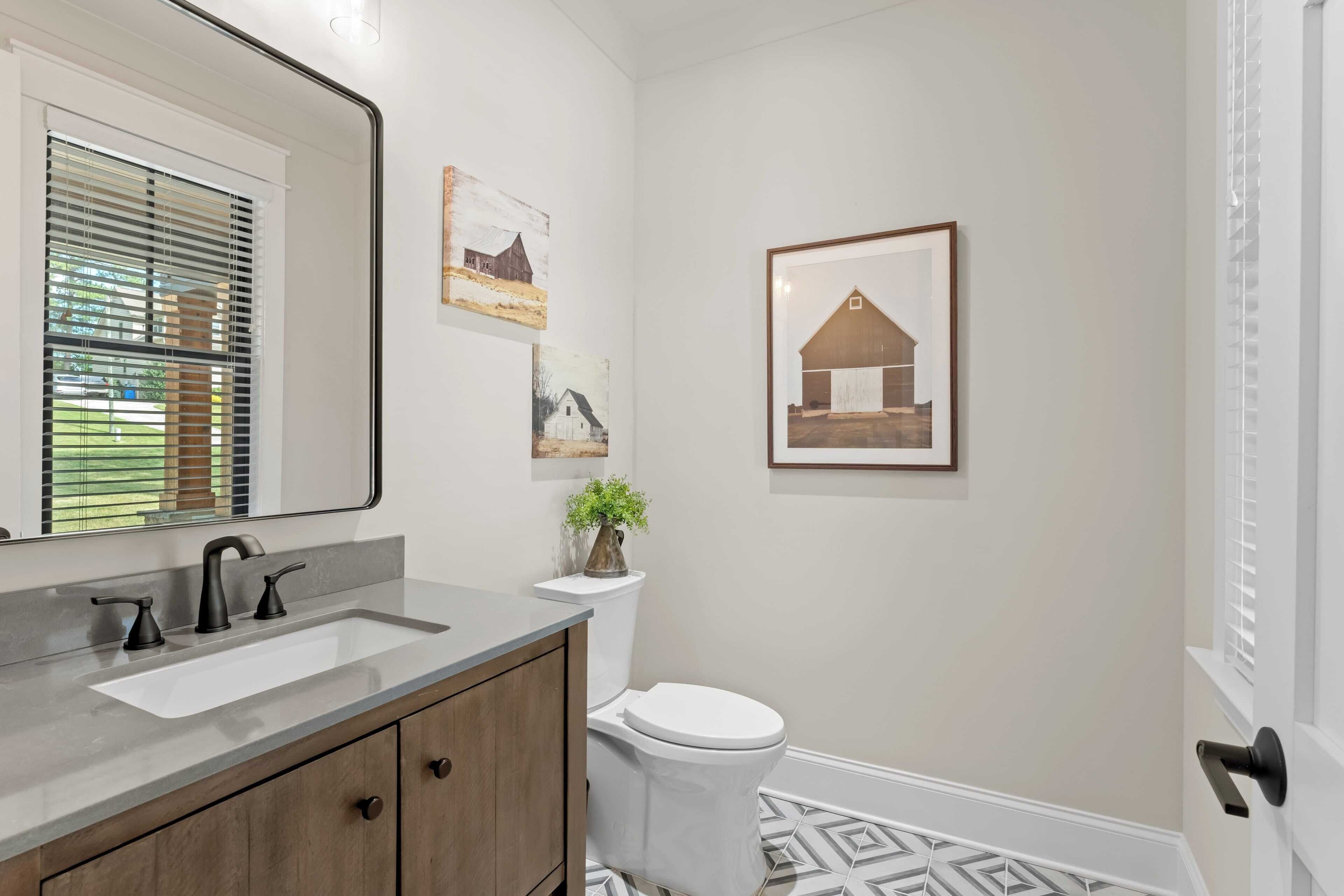 A bathroom with a large mirror, a sink, a toilet, and a framed picture on the wall.