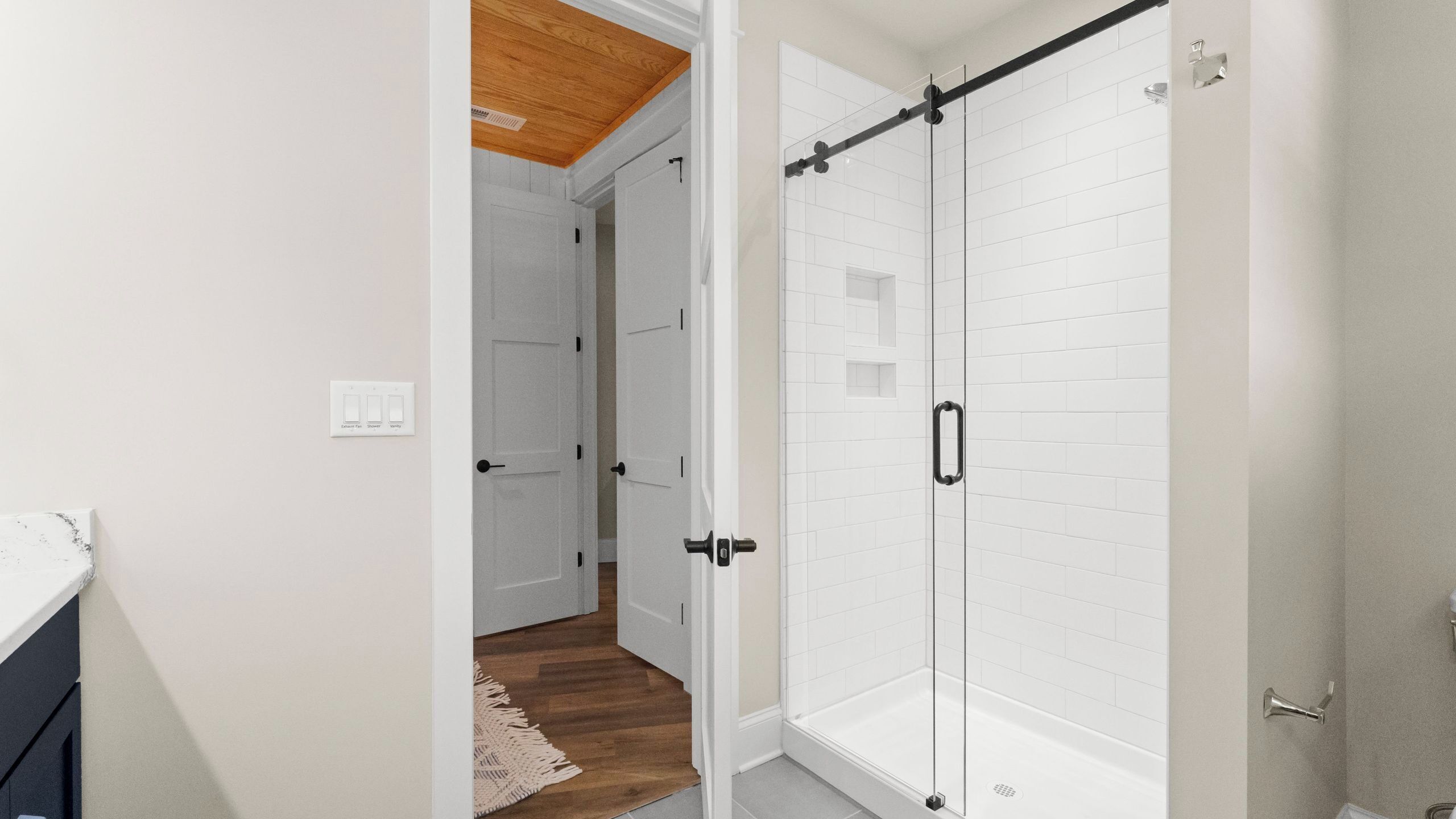 Une salle de bain avec des carreaux de céramique blancs rectangulaires, une douche en verre et un plafond en bois.