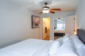 A bedroom with a bed, a ceiling fan, a door leading to another room, and a framed picture on the wall. - Echo Beach 2 Bed Lake View and Walkable to Beach (Harrison Hot Springs)