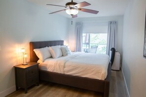 A bedroom with a bed, nightstand, ceiling fan, and window with curtains.