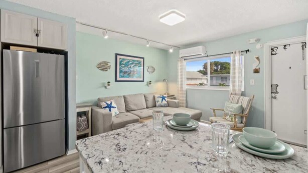 A modern kitchen with a large marble island, stainless steel refrigerator, and light blue walls. - Beach Pad | Pool | Walk to the beach (Cape Canaveral)