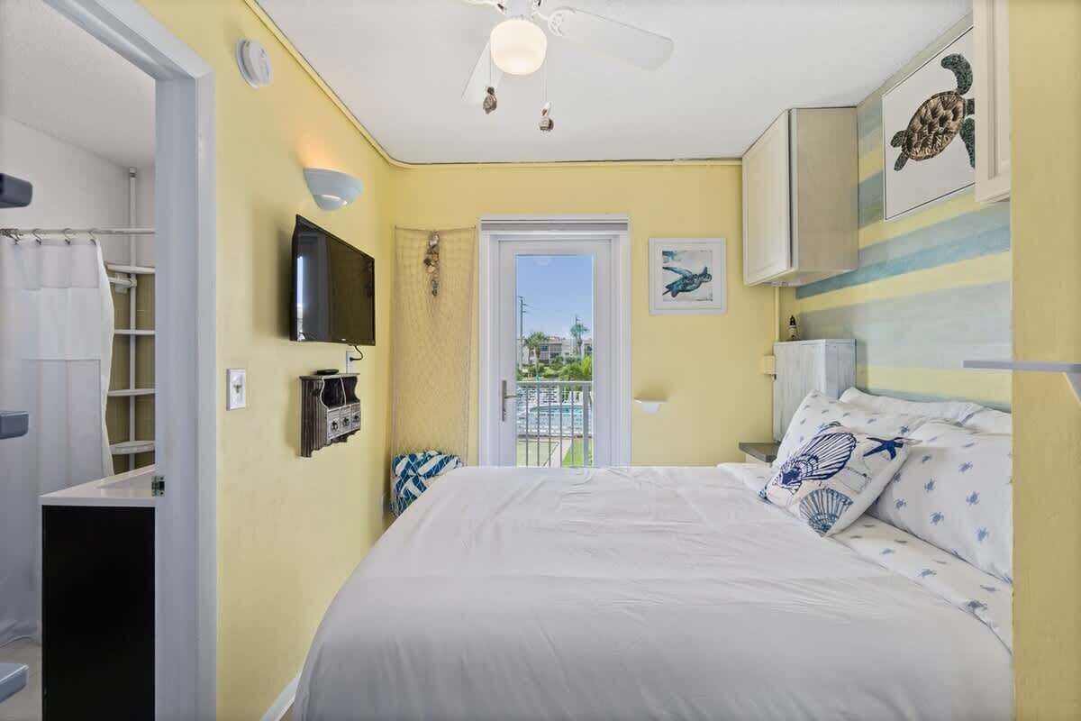 A bedroom with a bed, a ceiling fan, a TV, and a door leading to a balcony.