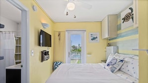 A bedroom with a bed, a ceiling fan, a TV, and a door leading to a balcony. - Beach Pad | Pool | Walk to the beach (Cape Canaveral)