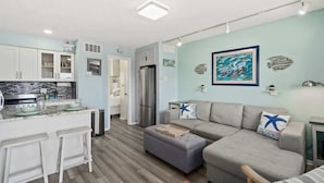 A modern kitchen with white cabinets and a marble countertop, a grey sofa with starfish pillows, and a wooden bench. - Beach Pad | Pool | Walk to the beach (Cape Canaveral)