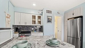 A modern kitchen with white cabinets, a stainless steel refrigerator, and a granite countertop. - Beach Pad | Pool | Walk to the beach (Cape Canaveral)