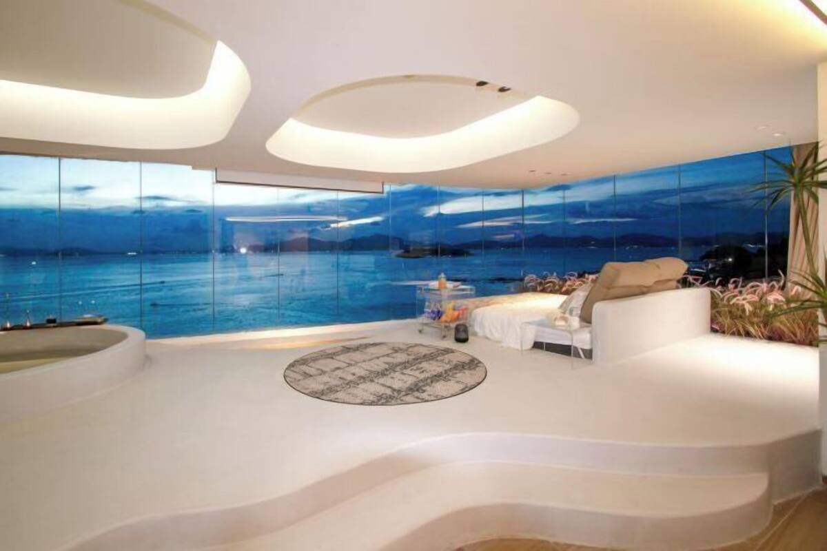 A modern interior with a panoramic sea view, a circular seating area, and a unique ceiling design.