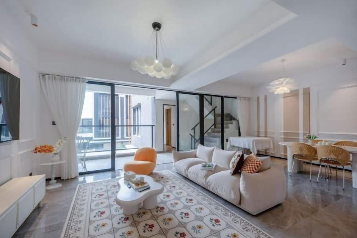 A modern living room with a sofa, coffee table, and chairs, a staircase, and a dining area.