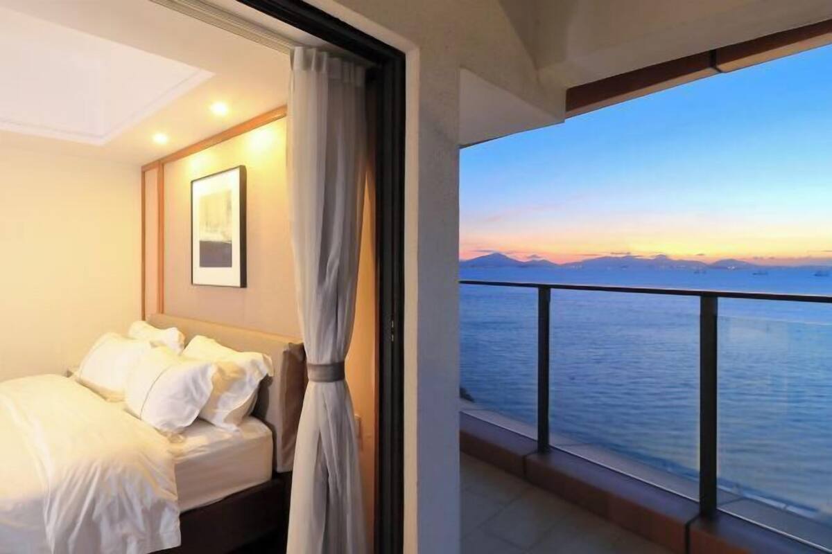 A hotel room with a bed, a curtain, a framed picture, and a balcony with a view of the sea and mountains.