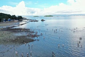 A coastal beach with people wading in shallow water, a pier, and distant land. - Island Skylight Resort (Huidong)