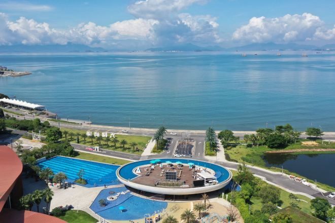 Un hotel con piscina, una fuente circular y vista al mar.