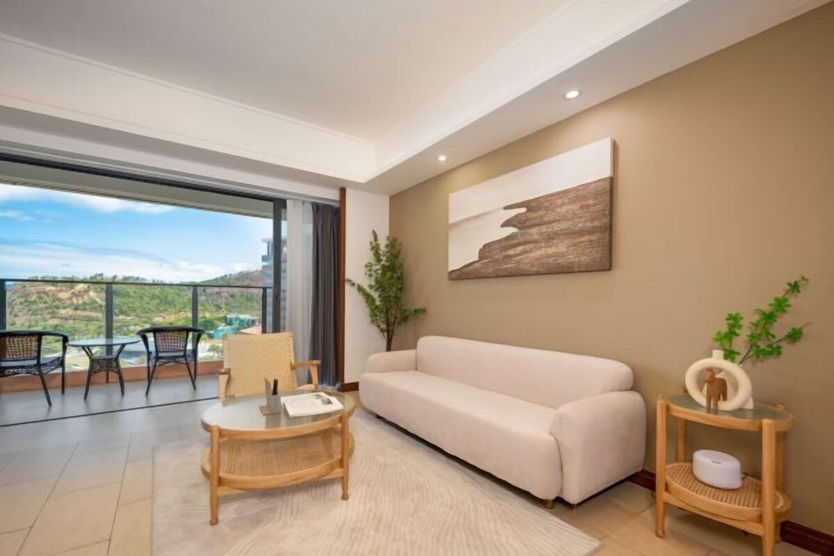 A modern living room with a sofa, a round coffee table, and a side table. There is a large window offering a view of the outdoors.