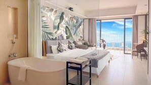 A modern hotel room with a large bed, a bathtub, a balcony with a view, and a tropical-themed wall mural. - Island Skylight Resort (Huidong)