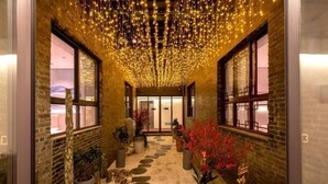 A corridor with brick walls, large windows, and a ceiling adorned with string lights. - Yongle Inn (Yangzhou)