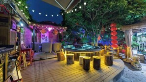 An outdoor seating area with wooden tables and stools, surrounded by greenery and decorative lanterns. - Yongle Inn (Yangzhou)