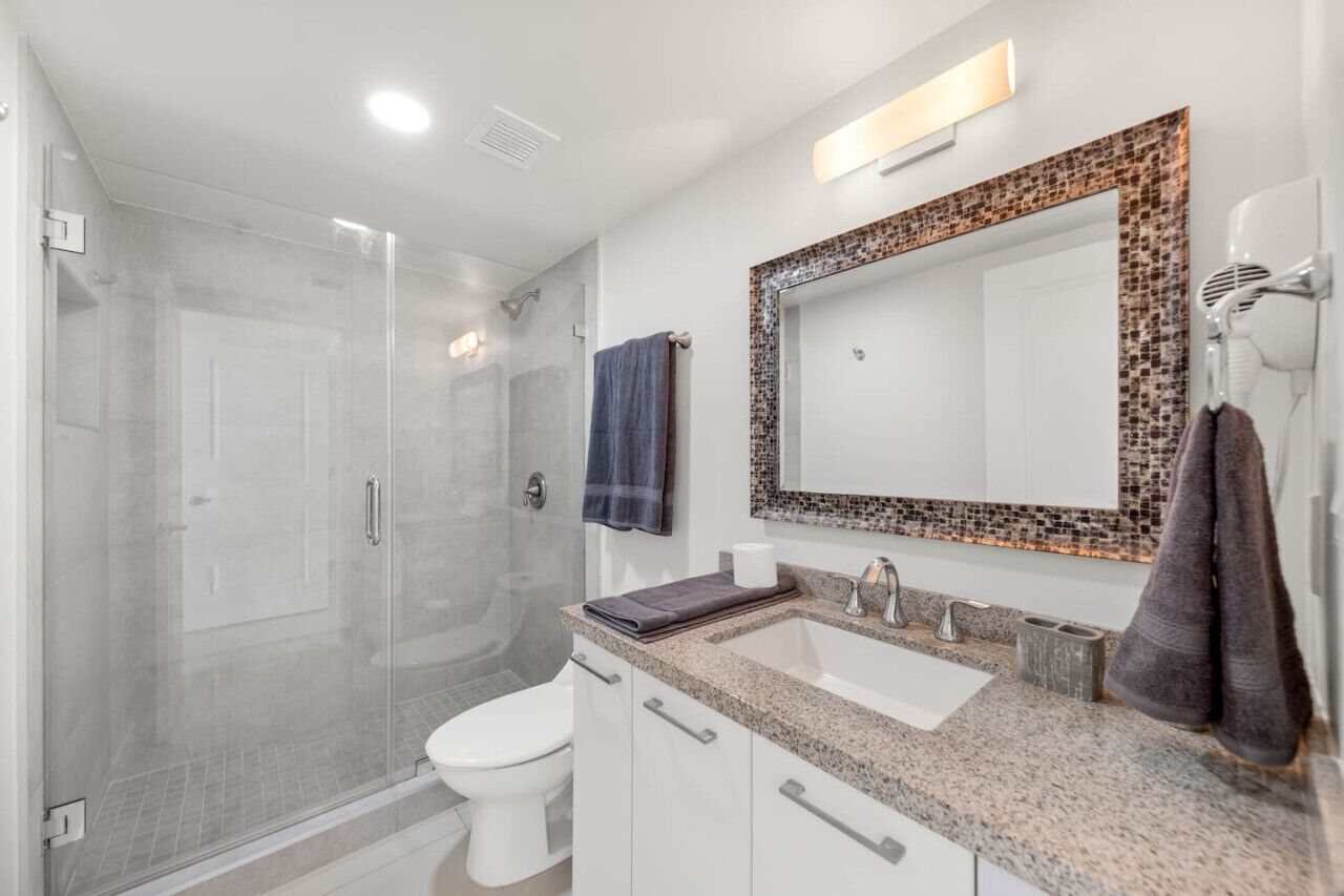 A modern bathroom with a glass-enclosed shower, a white toilet, a sink with a mosaic-tiled vanity, and a towel rack.