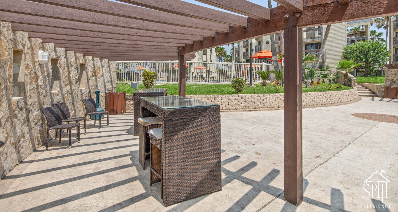 Un patio al aire libre con mobiliario de mimbre, una mesa con cubierta de vidrio y una pared de piedra.