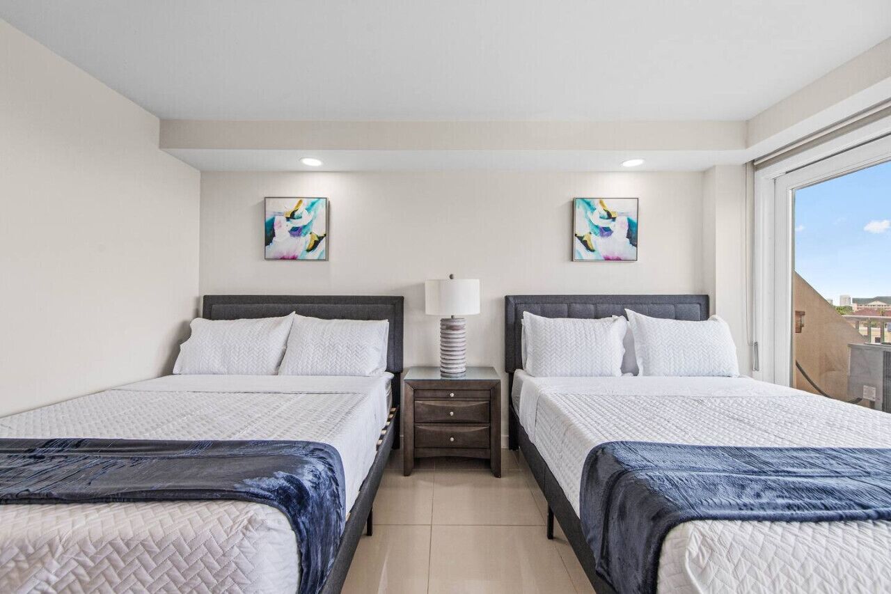 A hotel room with two beds, a nightstand with a lamp, and two abstract paintings on the wall.