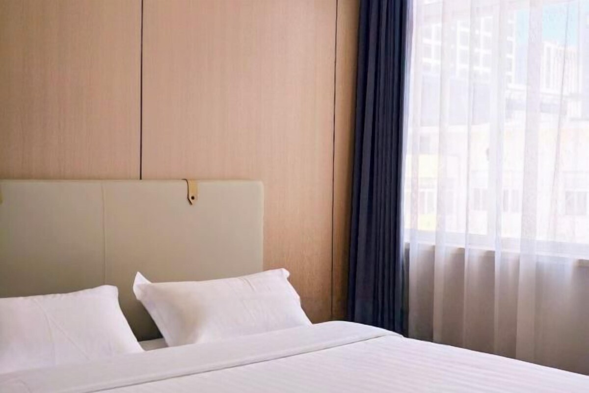 A hotel room with a bed, a headboard, and a window with sheer curtains.