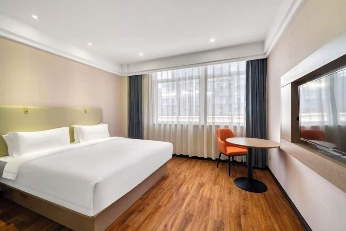 Ein Hotelzimmer mit einem Bett, einem kleinen Tisch mit Stuhl, einem Fernseher und einem Fenster mit Vorhängen.