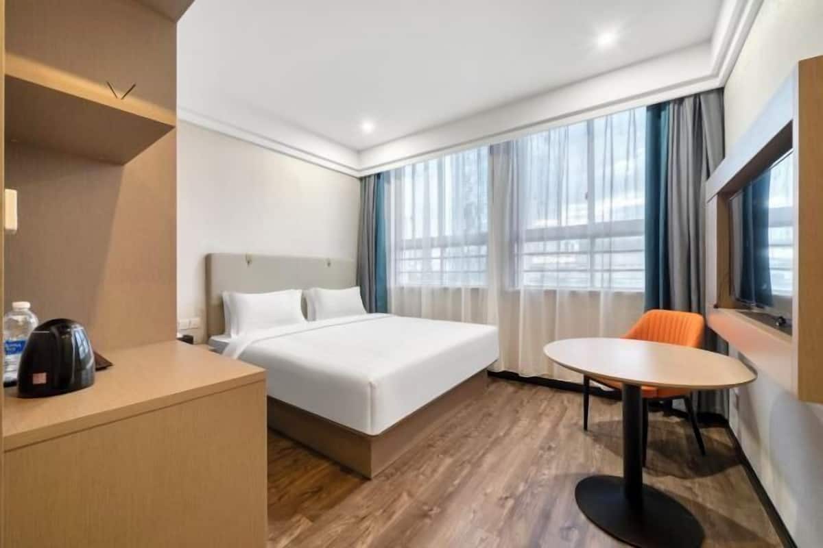 Ein Hotelzimmer mit Bett, Schreibtisch, Stuhl und einem fenster mit Vorhängen.