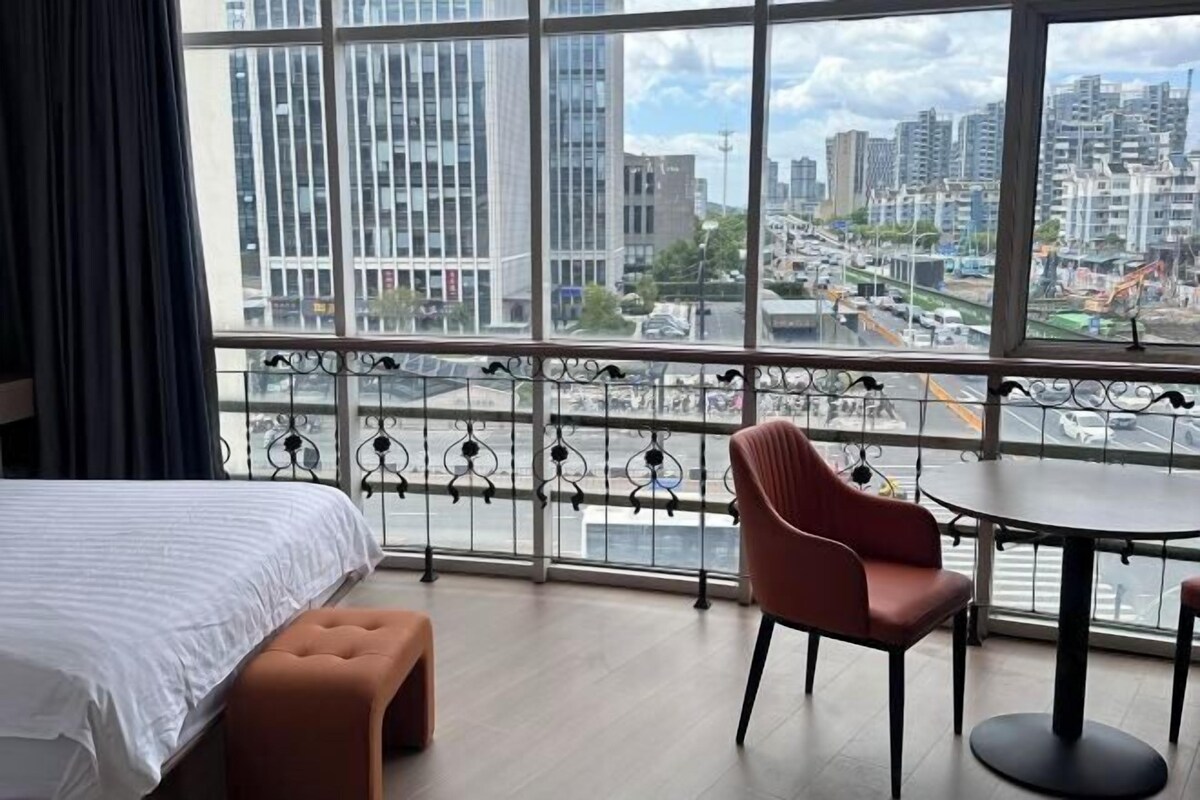 Hotellihuone, jossa on suuri ikkuna, sänky, tuoli ja pieni pöytä.